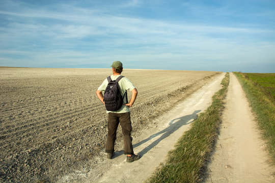 Man traveler with a backpack standing on a country road