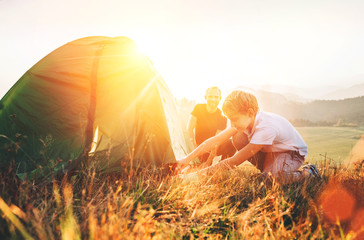 Father learn his son set up camping tent on sunset forest glade - obrazy, fototapety, plakaty