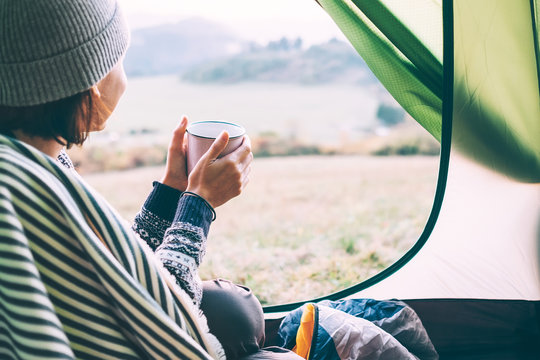 Woman with cup of hot tea sit in camping tent