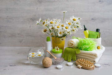 Spa composition with daisy flowers: cosmetic and bath products, accessories for massage and peeling on light background. Wellness concept, front view, copy space