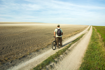 Fototapeta na wymiar Man traveler walking with a bike through a country road