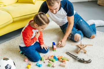 father and cute little son playing with wooden blocks together at home