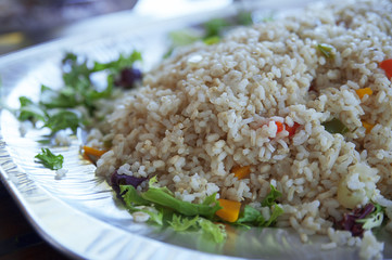 Healthy steamed brown, integral rice with vegetables on a large plate, served on its own or as a side dish, a delicious option for vegetarians or vegans, at a buffet bar, or self-service restaurant