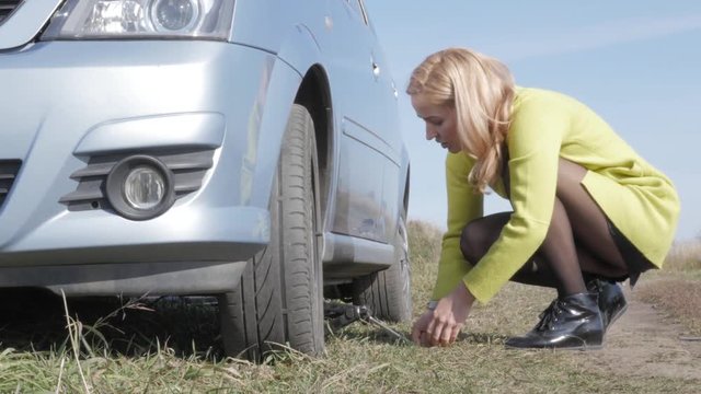 seductive blonde woman trying change wheel on a car on rural road. 4K