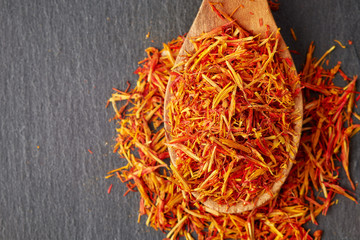 Safflower petals (Saffron substitute) in wooden spoon on black background. Top view with copy space