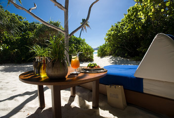 Luxury lunch served on private tropical beach hideaway, table set by cosy day bed