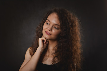 Attractive female with charming smile looking aside and touching face, having dreamy thoughtful facial expression. Portrait of gorgeous beautiful woman with long dark hair daydreaming indoors