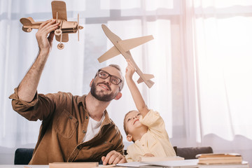 happy father and little son playing with wooden planes models at home
