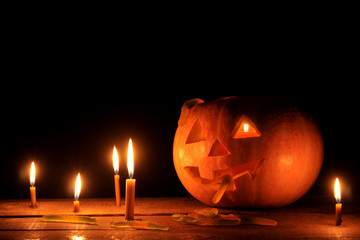 The concept of the holiday of Halloween. Halloween pumpkin head with candles inside and around on a wooden table on a black background