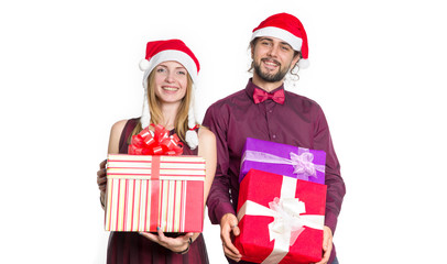 Happy couple of young people in Santa Claus hats and with boxes of gifts in their hands on a light background. Man and woman in a festive mood - New Year, Christmas, shopping for gifts.