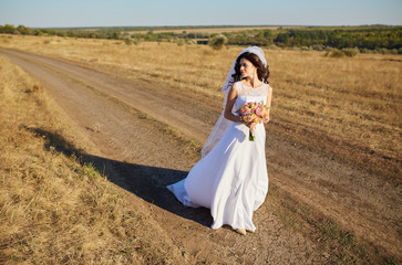 Fototapeta premium Beautiful smiling bride wearing a natural flower wreath and standing in the golden summer fields