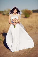 Fototapeta premium Beautiful smiling bride wearing a natural flower wreath and standing in the golden summer fields