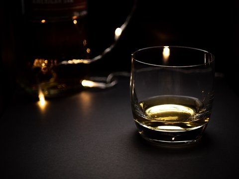 A low key image of a glass of whisky with fairy lights in the background