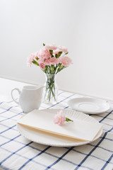 Table setting with dishes, cutlery and flowers on white background