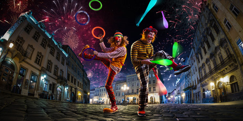 Night street circus performance whit two clowns, juggler. Festival city background. fireworks and Celebration atmosphere. - obrazy, fototapety, plakaty