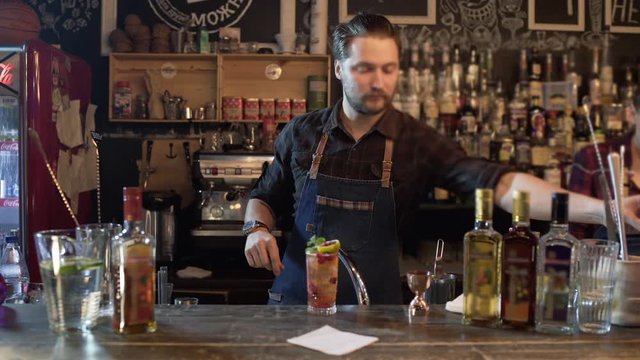 Professional bartender decorating cocktail with lime, raspberry and mint