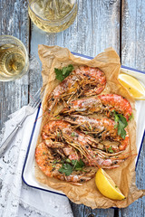 Traditional fried black tiger prawn with lemon and white wine as top view in a white casserole on a wooden blue board