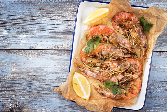 Traditional fried black tiger prawn with lemon as top view in a white casserole on a wooden blue board with copy space left