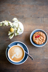 Top view on a beautiful stylish cup of coffee, as well as tasty cookies and a romantic bouquet of flowers on the background of a wooden table in a bright and cozy cafe