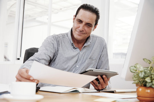 Confident enterpreneur examining contract and using digital tablet during work day at office