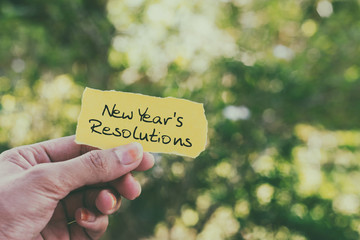 Hands holding piece of paper with text - New Year's resolutions.