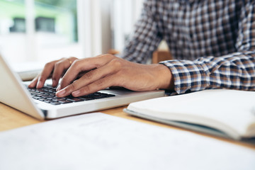 Close-up view of anonymous man in checked shirt sitting at table and typing on notebook