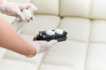 A woman cleans the leather sofa with a brush and detergent.
