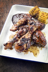 Traditional barbecue chicken drumsticks with corm and hot chili sauce as top view in a white fryer