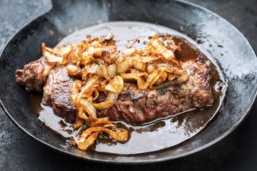 Traditional dry aged sliced roast beef with fried onion rings as closeup in a wrough-iron pan with brown sauce