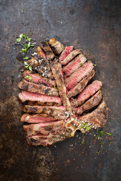Barbecue dry aged wagyu porterhouse steak sliced and decorated with spice and herbs as top view on an old rusty board with copy space
