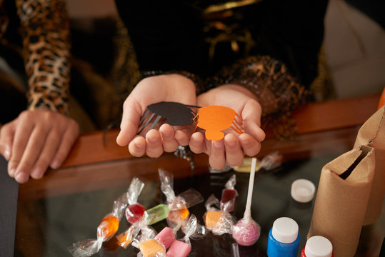 Close-up view of unrecognizable girls holding diy paper spiders over table with candies prepared for Halloween party