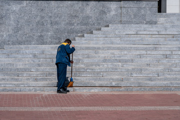 Minsk, Belarus, 2018. Man in uniform is sweeping stairs with broom on sunny day. Cleaning concept