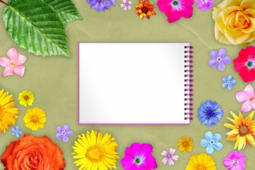 Beautiful flower frame with copybook in center on yellow kraft paper background. Floral composition of spring or summer flowers.