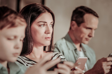 Deep in thoughts. Thoughtful brunette woman sitting between her males while looking forward