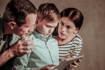 Negative emotions. Angry boy bowing head while playing game on tablet