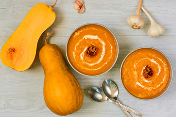 Spicy pumpkin soup with walnuts in the gray bowls decorated with sliced yellow pumpkin on the gray concrete background. Traditional autumn food or thanksgiving dish. Top view