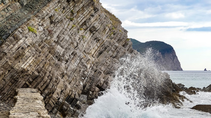 Unusual rugged coastal outcrop showing rock strata, with wave breaking over.  Isolated flora, with...