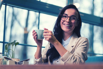 Join me. Happy brunette looking aside while leaning elbows on table