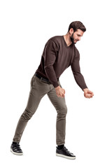 Naklejka premium A fit bearded young man in casual clothes tries to pull an invisible rope with all his strength from low grip.