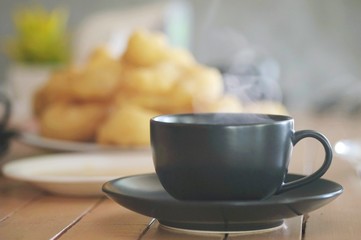 Hot coffee in ceramic black glass serve on wooden table in front of the chainess donut in the morning.
