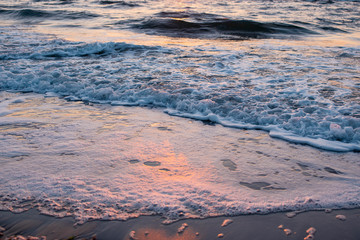 Sunrise and a beautiful cloudy sky early in the morning on the sandy shore on which the sea water beats and turns into foam