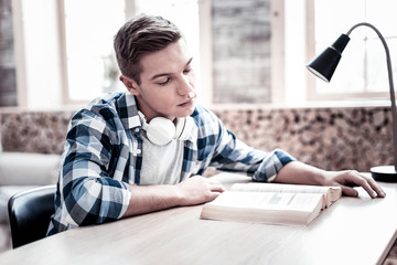 Reading alone. Calm tired young student getting ready for the exam and leaning his head while...