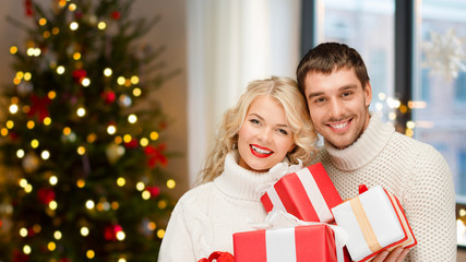 Obraz na płótnie Canvas holidays and people concept - happy couple with gifts at home over christmas tree lights background