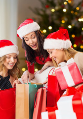 holidays and people concept - women in santa hats with gifts and shopping bags over christmas tree lights background