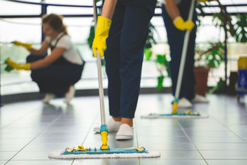 Close-up on professional cleaner with yellow gloves and mop wiping the floor
