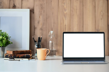 Laptop showing blank screen on a white wooden desk with a white poster and accessories