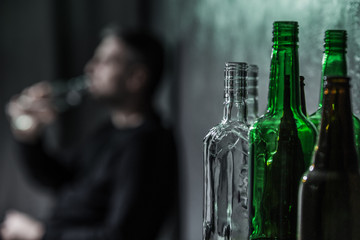 Close-up on bottles and blurred person drinking alcohol in the background