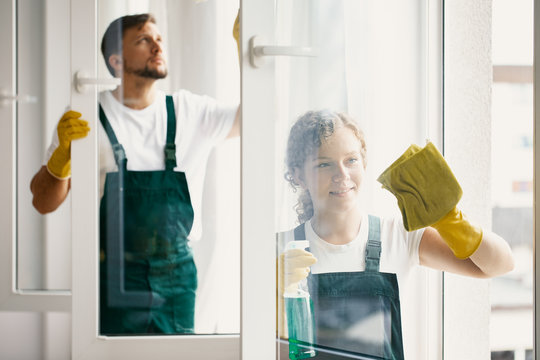 Man and woman in green overalls wiping windows while cleaning home