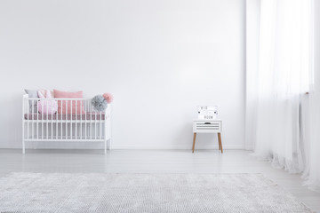 Carpet and cabinet in minimal white kid's bedroom interior with pink cushion in cradle. Real photo