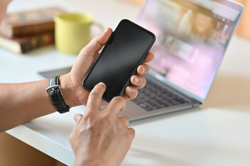 Male hands holding mobile phone in office.